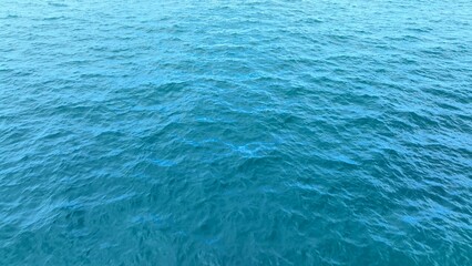 Obraz premium Aerial view reveals the serene ocean, with soft blue waves rippling across the surface, creating a natural, textured pattern that reflects the beauty of tropical waters. 