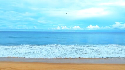 A vast horizon meets the cloudy sky above the calm tropical sea. The light waves ripple gently, lapping against the beach, creating a perfect harmony of nature and serenity.