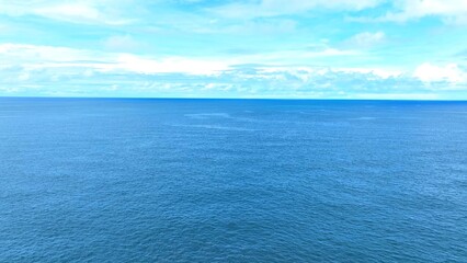 The aerial view reveals the endless stretch of tropical sea, where the water merges with the sky in...