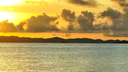 From an aerial perspective, the tropical sea at sunset appears to shimmer with shades of orange and purple, as the sun&rsquo;s final rays reflect off the water and disappear behind the mountains.
