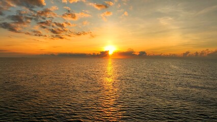 From above, the tropical sea glistens under the golden light of the setting sun. The clouds add depth to the scene, creating a peaceful yet dramatic portrayal of nature’s majesty.

