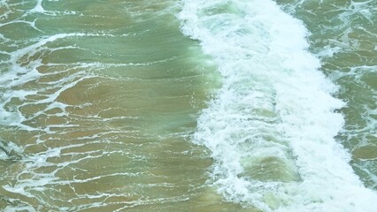 Foam bubbles form as the waves gently crash against the sandy shore. The clear blue water and frothy surface provide a refreshing and tranquil beach scene. Thailand.
