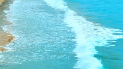 The ocean waves roll onto the shore, creating a foam-filled surface. The clear water blends with the white froth, capturing the peaceful movement of the sea in this coastal scene. Thailand.
