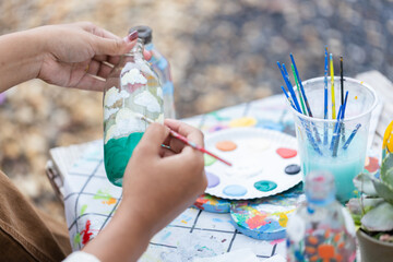 Person creates sustainable and ecofriendly craft art by painting clouds and sky on glass bottle...