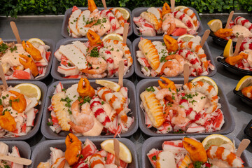 Sea street food for tourists on fish market on promenade in Oostende, Belgium, plastic box with variety of sea shells, shrimps, crab sticks, smoked fish
