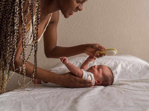 Happy mother brushing hair of playful babbling newborn