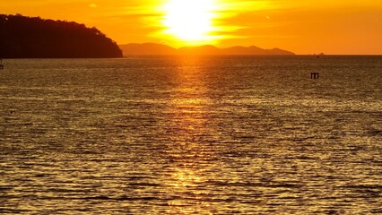 An aerial shot of a golden sunset over the ocean, with soft light reflecting on the water and mountains framing the horizon. Perfect for promoting nature reserves, beach holidays, and relaxation.
