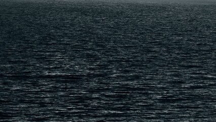 A striking aerial shot of the ocean's dark surface, with gentle ripples under a moody sky, ideal...