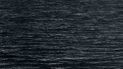 A dramatic aerial view of the dark, rippling ocean, captured in monochrome tones, evoking a sense...