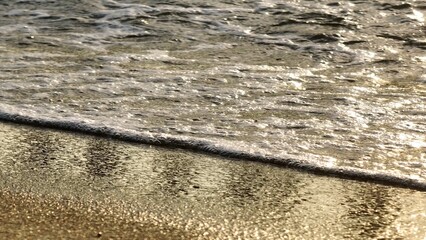 A mesmerizing close-up of golden sand with foamy waves washing ashore, capturing the calm and tranquility of the beach, ideal for nature, beach, and peaceful getaway themes. Phuket, Thailand.
