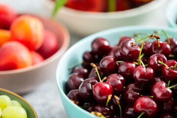 Cherries in a bowl surrounded by various fruit bowls on table