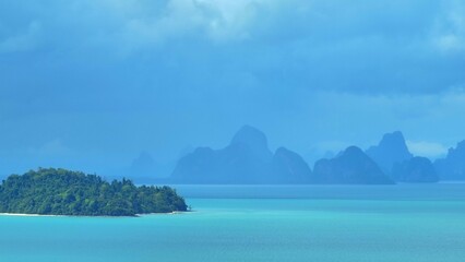 A dramatic aerial view of mountains in the distance, covered in mist and rain clouds, with the turquoise ocean beneath, creating a stunning and atmospheric coastal storm scene. Phuket, Thailand.
