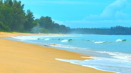 The soft, foamy waves touch the sandy beach, creating ripples in the turquoise water under the bright sky, embodying the calmness and natural beauty of a tranquil coastline. Phuket, Thailand.
