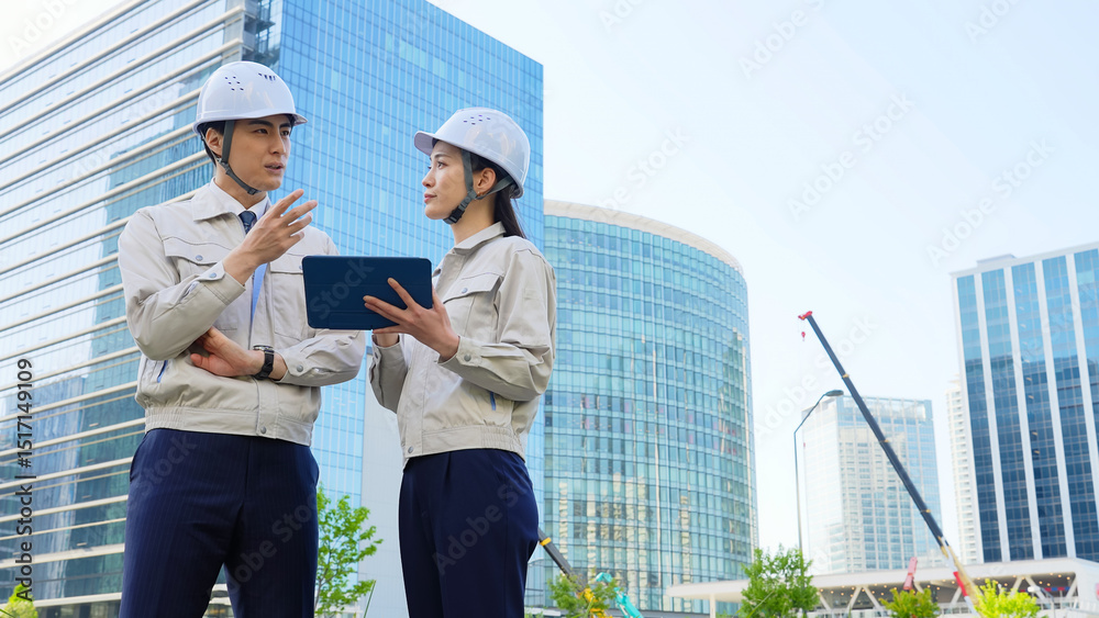 Poster 建設現場でタブレットを見ながら打ち合わせする男女エンジニアのグループ