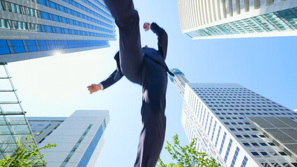 新緑の街でジャンプする男性ビジネスパーソンのアオリ構図