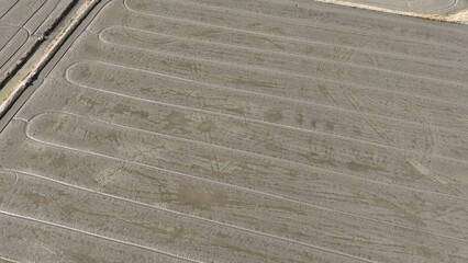 The preparation of a rice field is visible from an aerial perspective, with a series of smooth, parallel lines cutting across the wet soil, ready for planting. Thailand.
