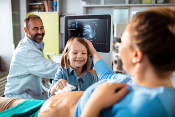 Pregnant woman with daughter and doctor during ultrasound appointment at clinic