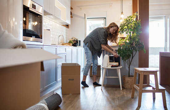 Young woman organizing items and unpacking boxes in new home kitchen - Powered by Adobe