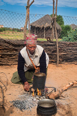 village rural ,portrait of african old woman, cooking in outdoors kitchen in front of a house with thatched roof , countryside living,