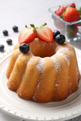 Tasty Bundt cake with powdered sugar and berries on light grey table, closeup