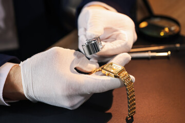 Appraiser with loupe evaluating luxury wristwatch at table, closeup