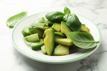 Cut ripe green avocado and basil on white marble table, closeup