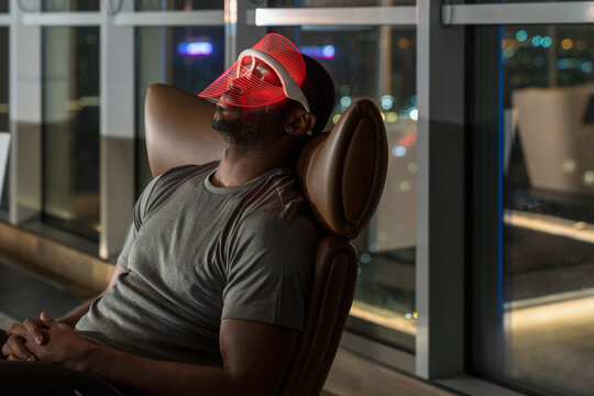 Man Using LED Light Therapy Mask in Modern Apartment