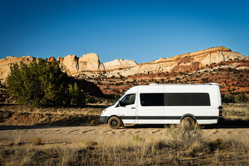 Camper van parked on a dirt road with Peekaboo Rock in the background in the Waterfold District of Capitol Reef National Park