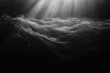 Dramatic monochrome image of ocean waves with rays of light breaking through clouds