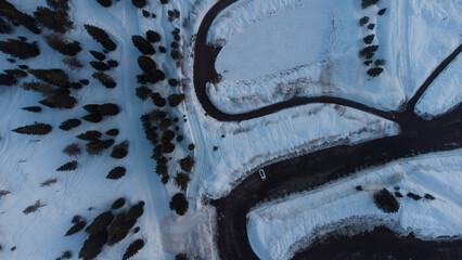  View of Snowy Curved Mountain Road with Single Car Driving Through Winter Landscape