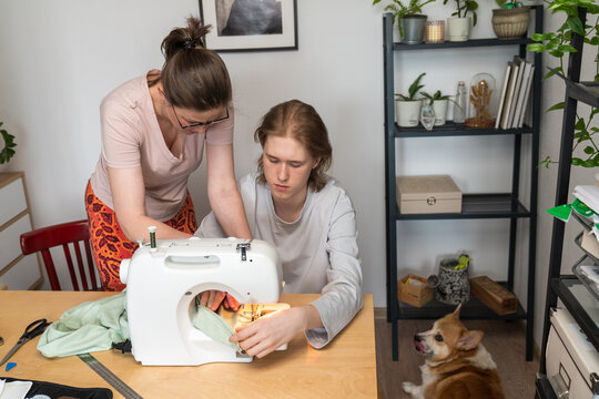 Mother Helping Son Sew at Home with Dog Nearby