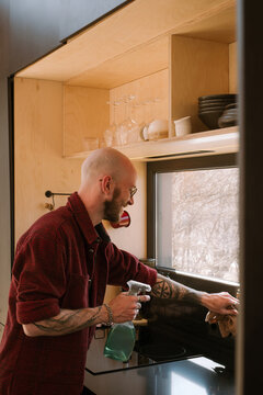 Man cleaning kitchen at home with spray bottle and cloth