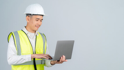 Smiling young Asian engineer or worker working with laptop in studio on grey background.