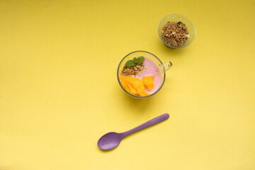 Yogurt with mango and granola in glass on yellow background