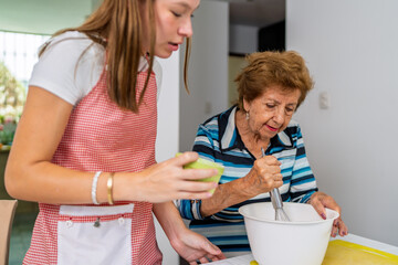 Grandmother whisking ingredients while granddaughter assists in the kitchen