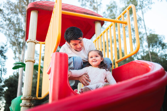 Father helping daughter going down slide in playground