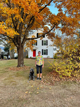 mature woman posing with dog in front of house in the fall 