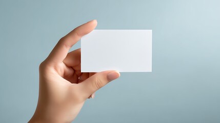 Fototapeta premium A Hand Holds A Rectangular White Card Against A Light Blue Background, branding and design element