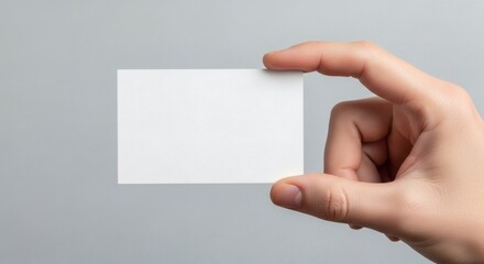 Fototapeta premium A hand holding a blank white card against a gray background for mockup and presentation purposes Mockup tamplete