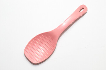 A pink, perforated rice spoon, possibly made of silicone or plastic, lies diagonally on a plain white surface.