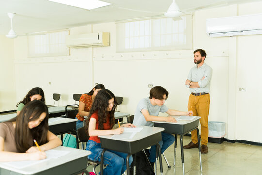 High school students taking exam with teacher supervising in classroom