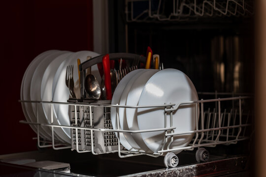 Open dishwasher with clean dishes in morning sun rays