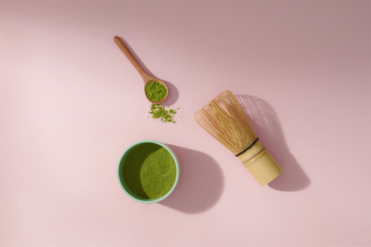 green tea powder bowl, wooden spoon, bamboo whisk on pink backdrop