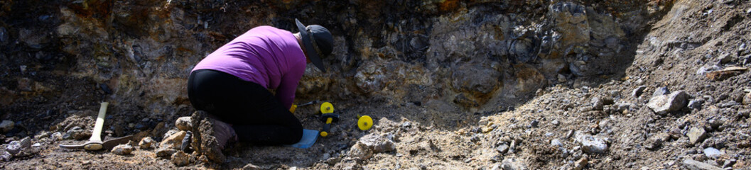 Mature woman rockhounding in Central Oregon, thunderegg pit with tools for digging, recreational hobby hunting for pretty rocks, sledgehammer, gloves, hammer, and pick
