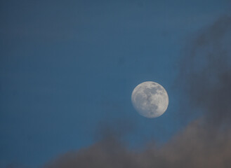 Detailed moon phase against a clear blue and cloudy sky.
