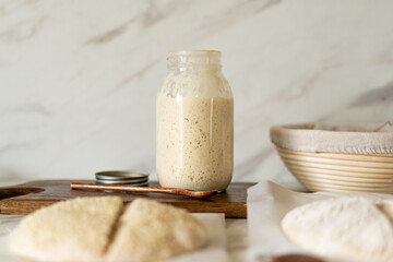 Freshly prepared sourdough bread dough rests on parchment near a container of active starter and a mixing bowl, showcasing the art of home baking.