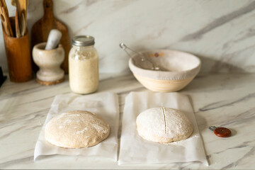Fototapeta premium Freshly prepared sourdough bread dough rests on parchment near a container of active starter and a mixing bowl, showcasing the art of home baking.