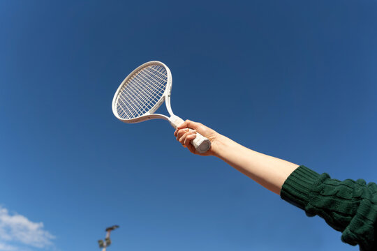 Hand holding tennis racket against blue sky