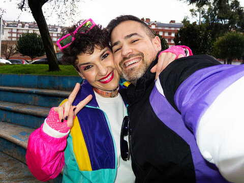 Couple wearing eighties costume taking selfie and making victory sign