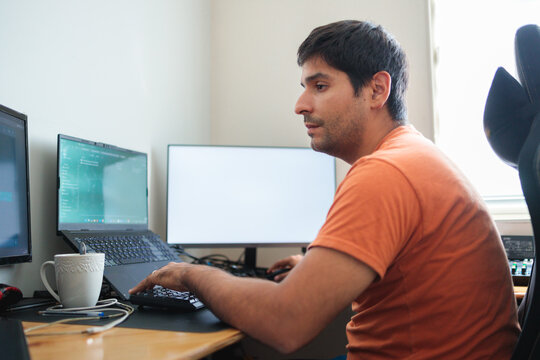 Focused latin man working from home on multiple screens